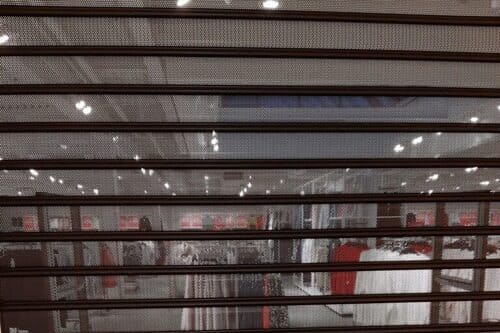 Perforerad ståljalusi med genomsikt monterad framför butiksentré i galleria.